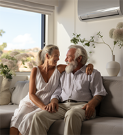A couple in their golden age sitting on a couch being cooled by an air conditioning unit